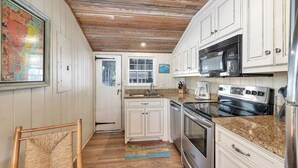 Una cocina con armarios blancos, un horno de acero inoxidable, un microondas y techo de madera.