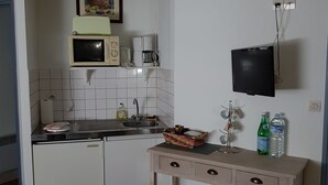 Eine kompakte Küche mit Mikrowelle, Kaffeemaschine und kleinem Kühlschrank. Ein Holztisch mit Schubladen und Ablagefläche darunter.