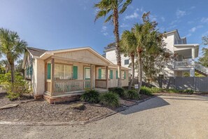 A two-story house with a covered porch, surrounded by palm trees and a gravel driveway.