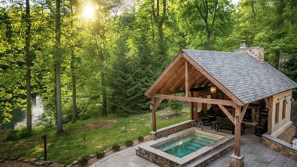 Une cabane en bois avec une piscine en pierre, entourée d’une forêt.