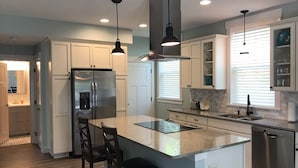 A modern kitchen with white cabinets, a stainless steel refrigerator, a central island with bar stools, pendant lighting, and a dishwasher. - Beautiful luxury 2 bedroom private   Cottage (Dunedin)