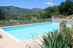 Une piscine entourée d’une clôture en bois, avec des chaises longues et une vue sur les montagnes.