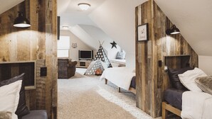 Una camera da letto mansardata accogliente, con pareti in legno, un soffitto spiovente, un letto, una scrivania e un televisore.