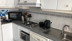 Pieni, käytännöllinen keittiö, jossa on valkoiset kaapit, mikroaaltouuni, liesi ja pesuallas.