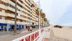 A beachfront hotel with multiple floors, outdoor seating, and a sandy beach in the background.