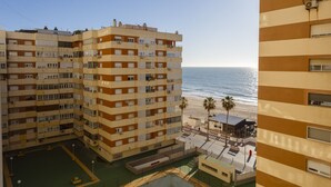 A multi-story residential building with balconies, a pool area, and a view of the beach.