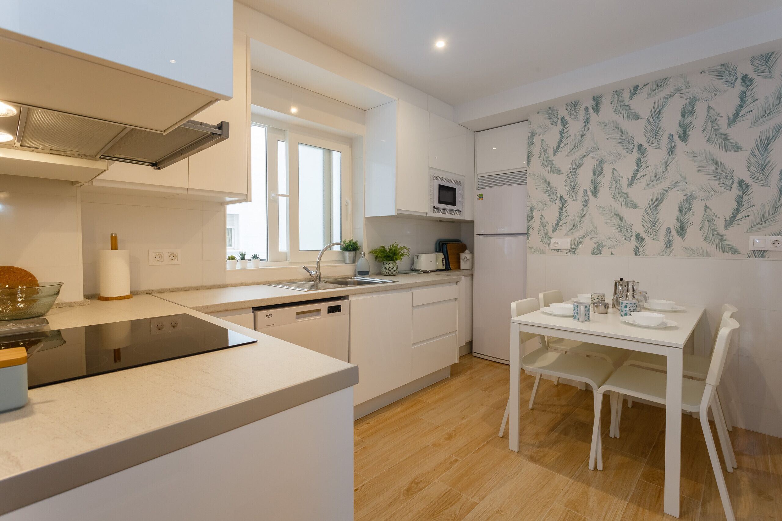 Una cocina moderna con armarios blancos, microondas integrado y un comedor con mesa y sillas blancas.