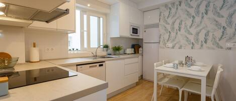 Una cocina moderna con armarios blancos, microondas integrado y un comedor con mesa y sillas blancas.