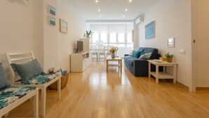 A spacious living room with a sofa, a coffee table, and a TV stand. There is a dining area with a table and chairs in the background.