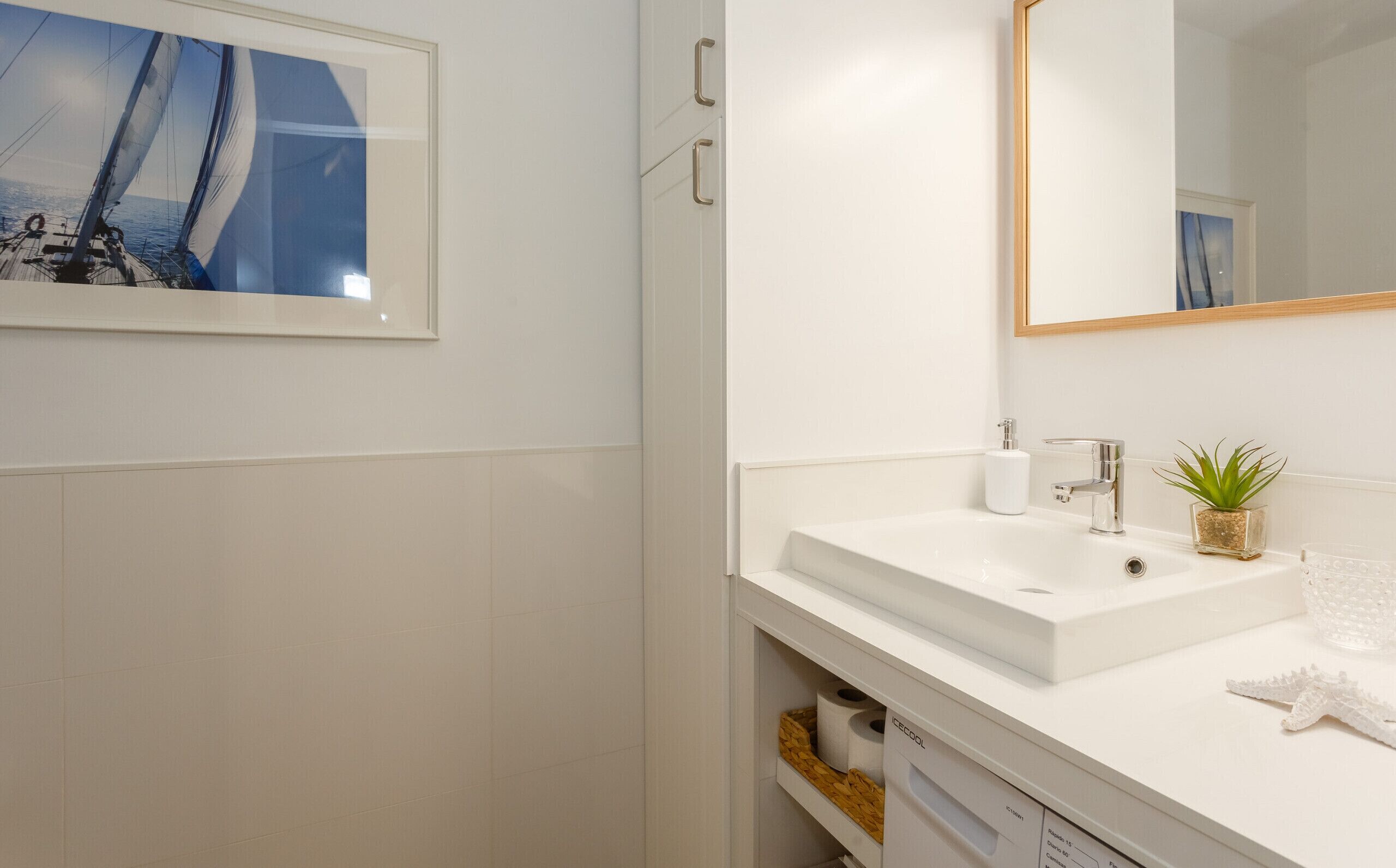 Een moderne badkamer met een witte wastafel, een spiegel en een lijst met een foto van een zeilboot.