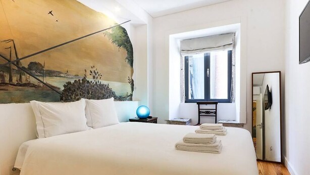 Une chambre d’hôtel avec un grand lit, un tableau au mur, une fenêtre avec des rideaux et un téléviseur posé sur un meuble.