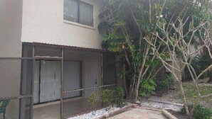 Una casa con un porche techado, una ventana y un árbol en el jardín.