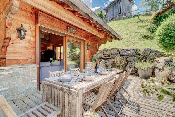 A wooden cabin with a stone wall and a dining area set up outside.