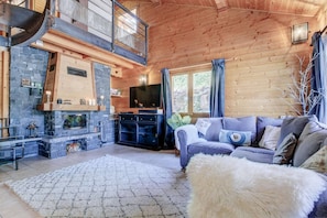 Een gezellig interieur van een chalet met een stenen open haard, een televisie en een comfortabele zithoek.