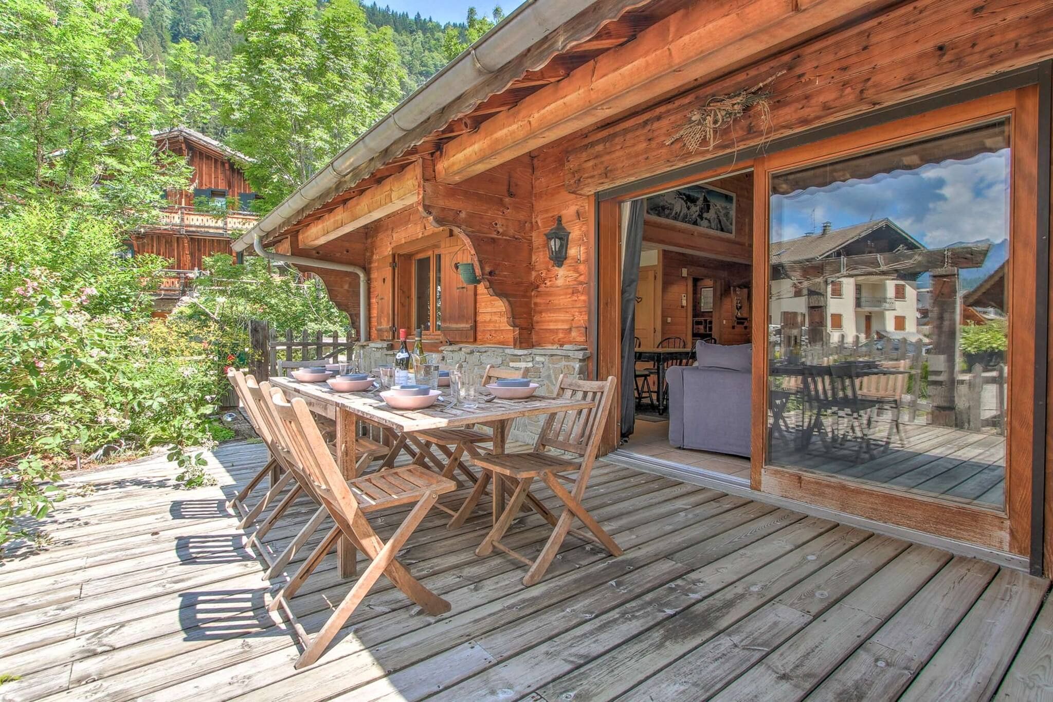A wooden cabin with a dining area on a deck, surrounded by greenery.