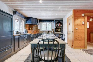 Una cocina moderna con comedor, que presenta una mesa grande dispuesta para seis personas, horno empotrado y ventana con vistas al exterior.