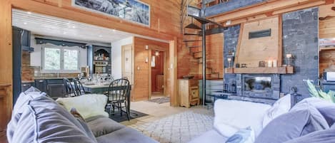 Interior acogedor de una cabaña con comedor, chimenea y escalera que conduce a un nivel superior.