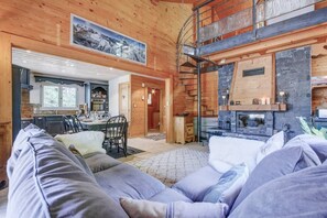 Ein gemütliches Blockhaus-Interieur mit Essbereich, Kamin und einer Treppe, die zu einer oberen Ebene führt.