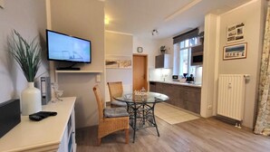 Ein modernes Wohnzimmer mit Flachbildfernseher, Esstisch mit Stühlen, einer kleinen Küchenzeile inklusive Mikrowelle und einem Heizkörper.