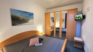 Ein Schlafzimmer mit Bett, Gemälde, Kleiderschrank, Fernseher und Nachttisch.
