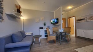 Ein Wohnzimmer mit einer Couch, einem kleinen Tisch, einem Fernseher und einem Sessel.