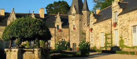 A historic stone building with multiple towers and a gravel courtyard.