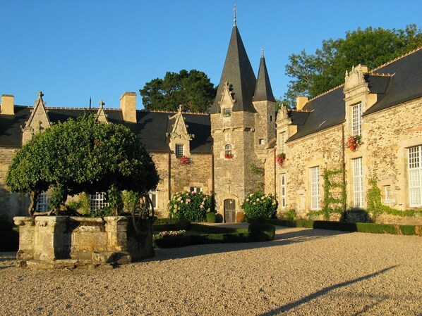 A historic stone building with multiple towers and a gravel courtyard.