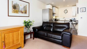 A living room with a black leather sofa, wooden cabinet, and a framed cityscape picture.