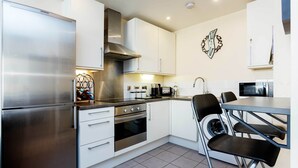 A modern kitchen with a stainless steel refrigerator, a built-in oven, a microwave, and a dining area with a table and chairs.