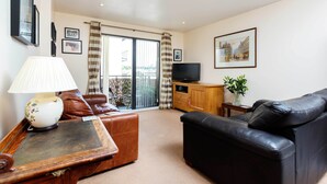 A living room with a sofa, a coffee table, a TV, and a balcony with curtains.