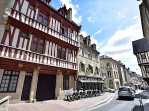 Une rue bordée de bâtiments traditionnels à colombages, un café avec une terrasse, et des voitures garées.