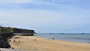 A beach with a rocky shoreline, a pier, and calm waters. - Martin pecheur - Ferme des Herils (Port-en-Bessin-Huppain)