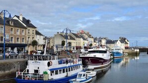A harbor with several boats docked along the waterfront, surrounded by buildings with balconies and a bridge in the background. - Martin pecheur - Ferme des Herils (Port-en-Bessin-Huppain)