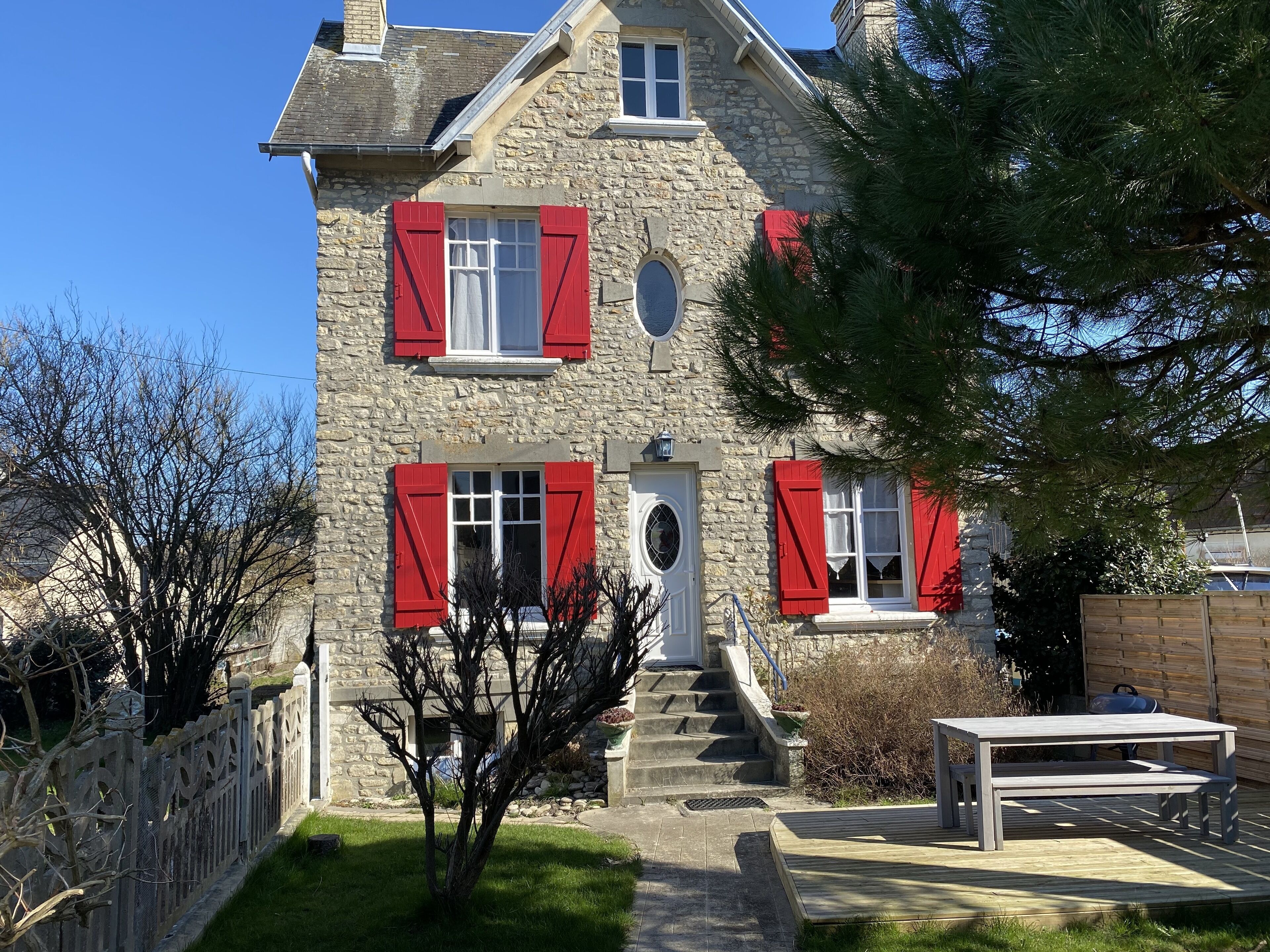 Una casa de piedra con contraventanas rojas, una puerta principal y una escalera que lleva a la entrada.