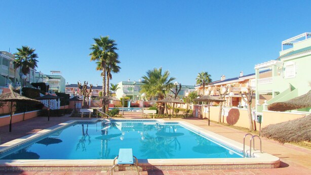 A swimming pool with lounge chairs and palm trees, surrounded by buildings with balconies. - bungalow with terrace (Gran Alacant)
