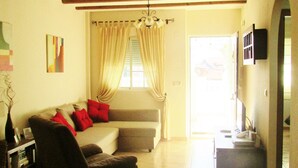 A living room with a sofa, armchair, and a television. There is a window with curtains, a chandelier, and a tiled floor. - bungalow with terrace (Gran Alacant)