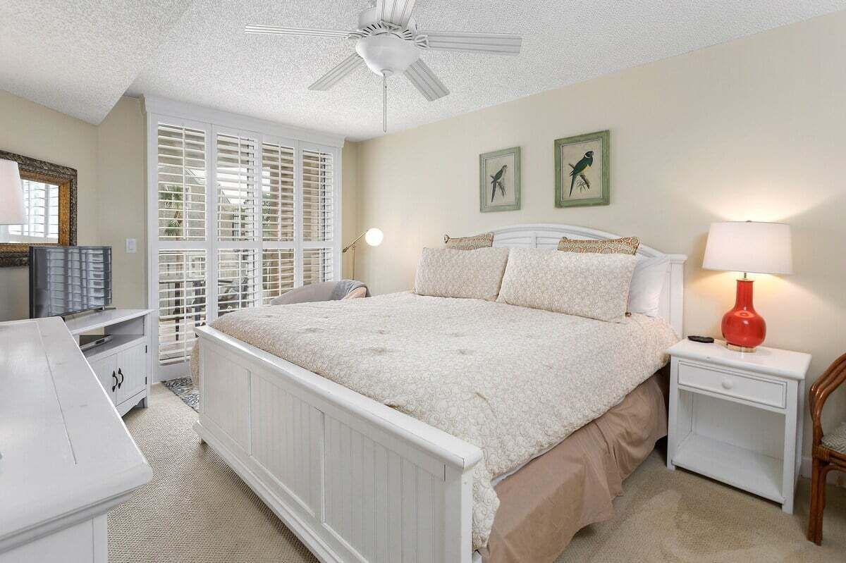 A bedroom with a white bed, a nightstand, a red lamp, and a ceiling fan.