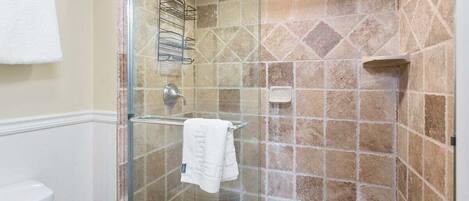 A glass-enclosed shower with a tiled wall, a white towel hanging on a rack, and a small shelf.
