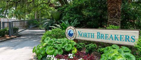 A sign for 'North Breakers' with a wooden board, surrounded by lush greenery and a palm tree.