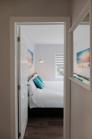 A bedroom with a bed, a window with blinds, a pendant light, and a painting on the wall.