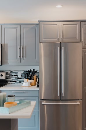 A modern kitchen with stainless steel appliances, light blue cabinets, and a white countertop.