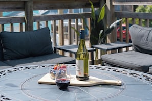 A round table with a wine bottle, a glass of red wine, and a small bowl of fruit.
