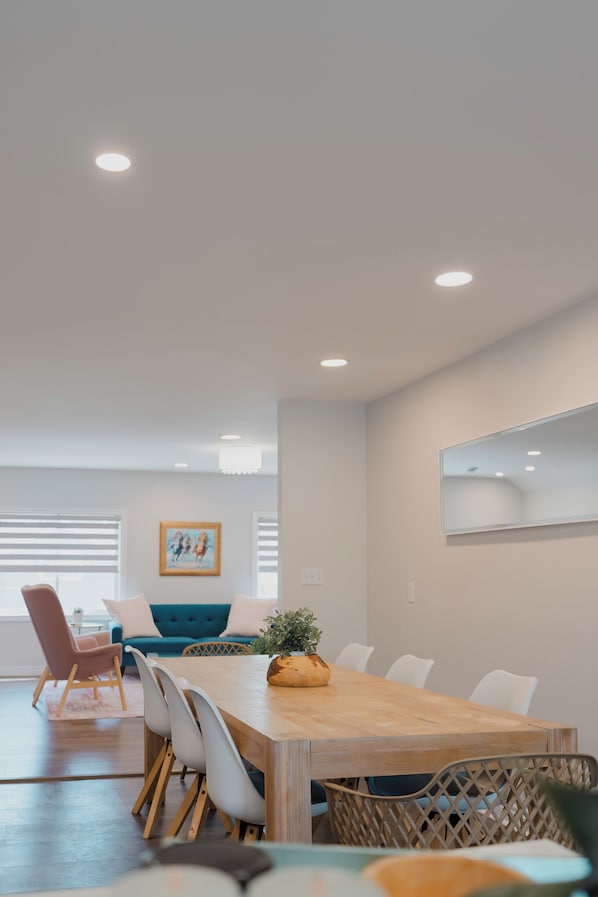A modern dining area with a wooden table, white chairs, a blue sofa, and a chandelier.