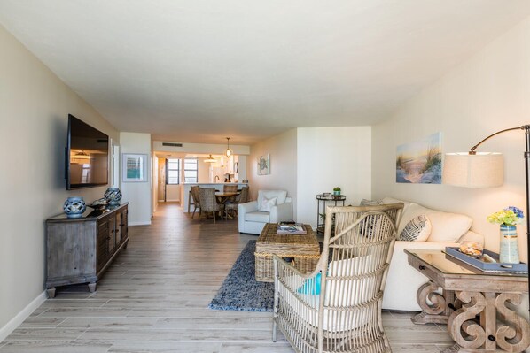 A spacious living area with a dining table, wicker chairs, a sofa, and a TV mounted on the wall. - South Seas Tower 3- 801: Beautiful Beach Condo! (Marco Island)