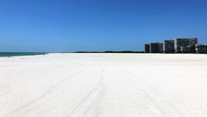 Ein weiter, sandiger Strand mit blauem Himmel und einer Reihe hoher Gebäude im Hintergrund.