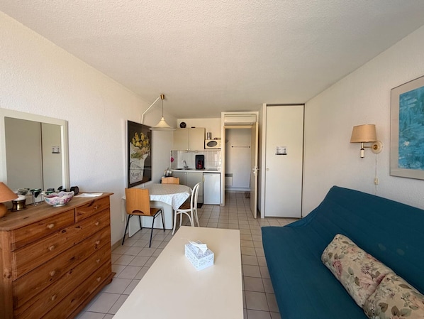 A compact living space with a kitchenette, a dining area, a sofa, and a wooden dresser.
