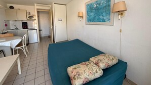 A room with a bed, a small table, a chair, a kitchenette, and a door leading to another room. - Air-conditioned studio with parking in Banyuls-sur-Mer near the sea (Banyuls-sur-Mer)