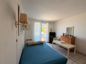 A bedroom with a bed, a dresser, a TV, and a window with curtains.