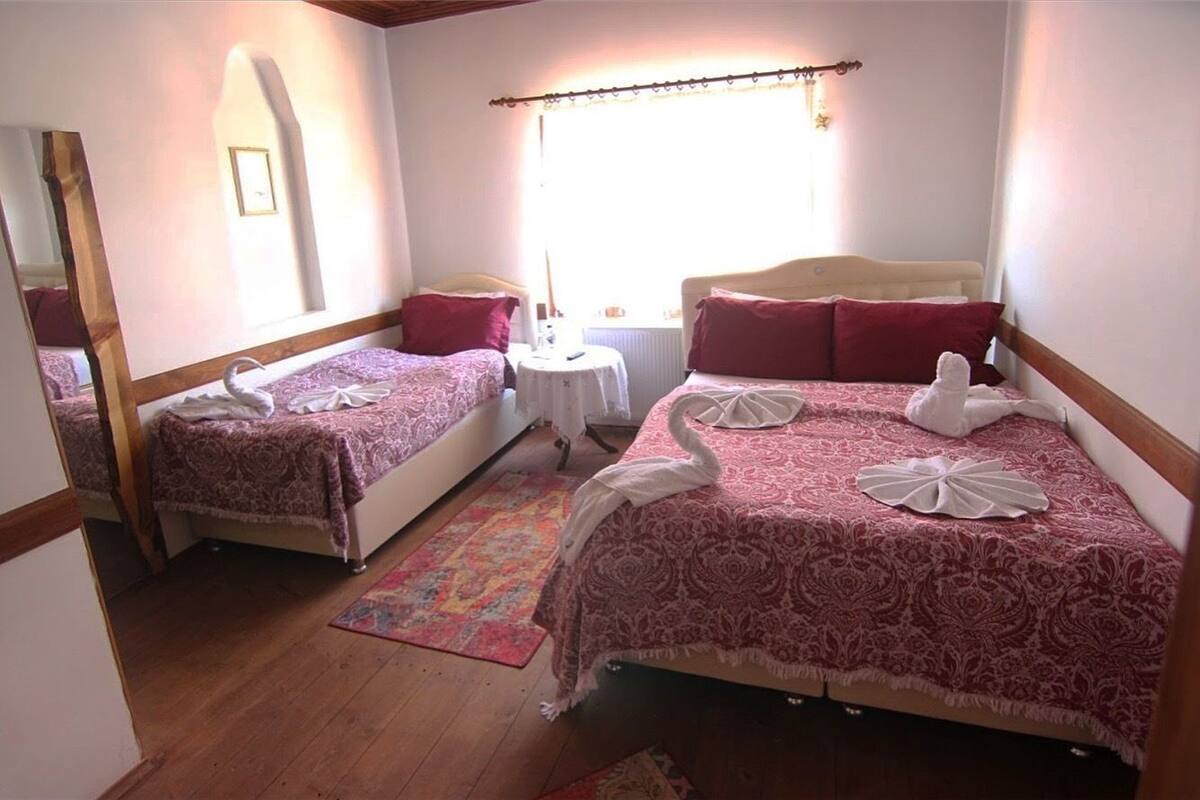 A hotel room with two beds, each with a swan-shaped towel, a small round table, and a window with curtains.