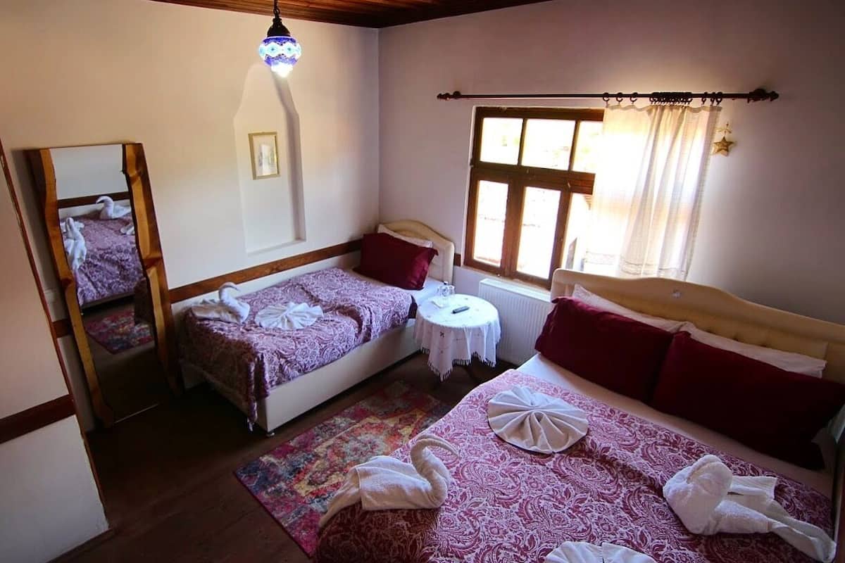 A room with two beds, a mirror, a small round table, and a window with curtains.